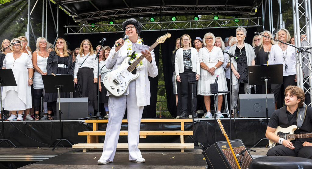Louise i Elvis-kostym med elgitarr på scen med kör.